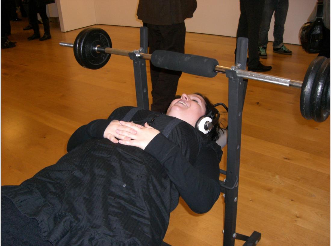 Photograph of someone listening to the First Flight project, headphones attached to a weightlifting bench.